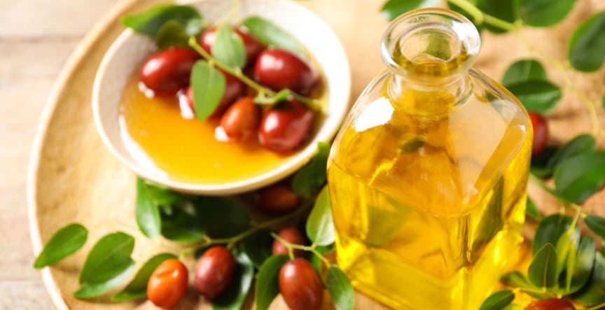bottle of jojoba oil with jojoba seeds and leaves on a wooden tray