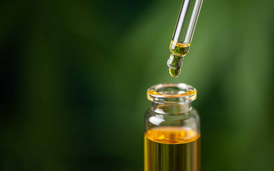 Dropper releasing essential oil into glass bottle with green background.