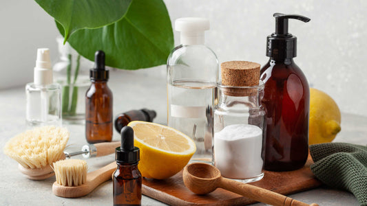 Natural skincare and cleaning ingredients including essential oils, lemon, baking soda, glass bottles, and wooden brushes on a countertop.